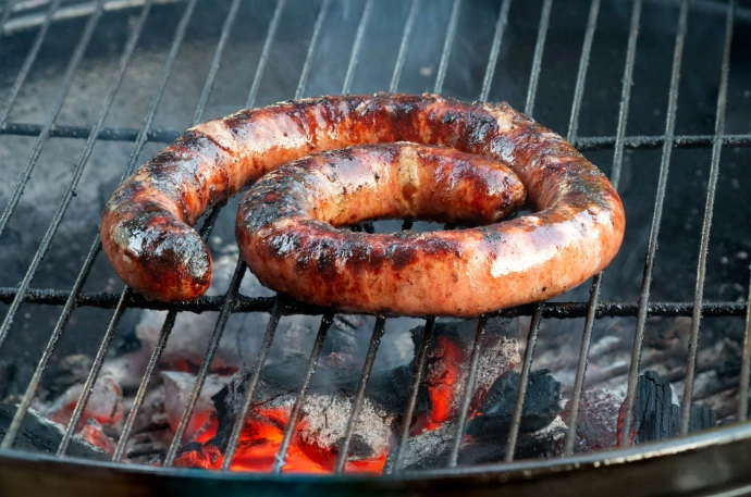 A coiled sausage cooking on a grill over hot coals